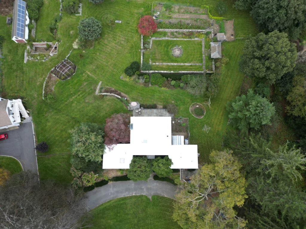 Aerial view of a large white flat roof surrounded by meticulously landscaped gardens and mature trees