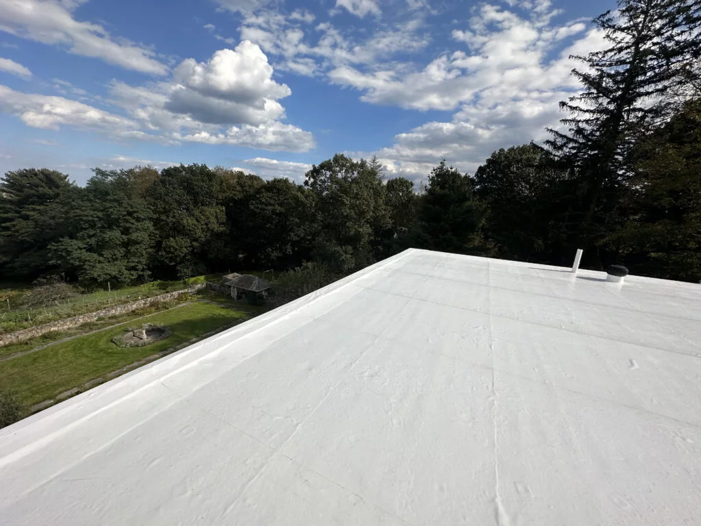 Newly installed white PVC flat roof with ventilation and a scenic view of trees and a cloudy sky