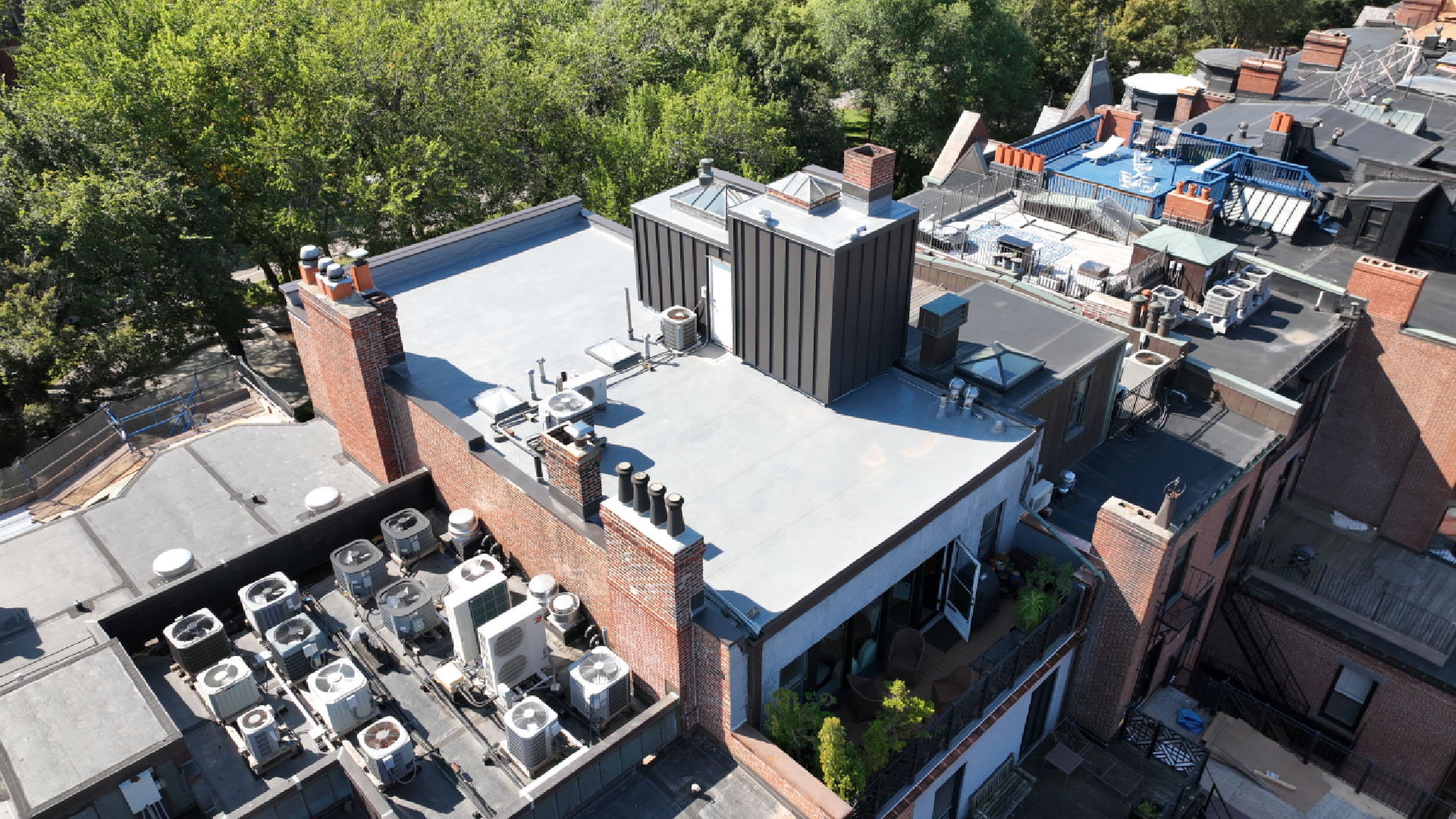 Flat roof repair Boston on a brick building with new white membrane roofing, skylight flashing, and waterproof coverage